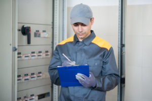 Electrician writing a document while inspecting a panel