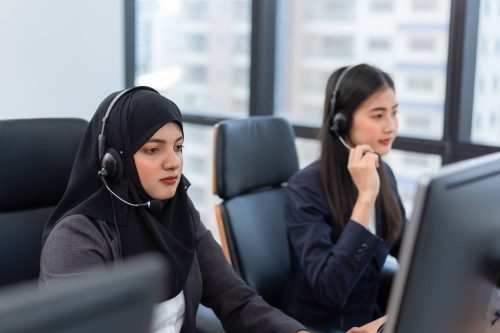 Arabian or Muslim woman works in a call center operator and customer service agent wearing microphone headsets working on computer in a call centre, talking with customer for assisting to resolve the problem with her service mind